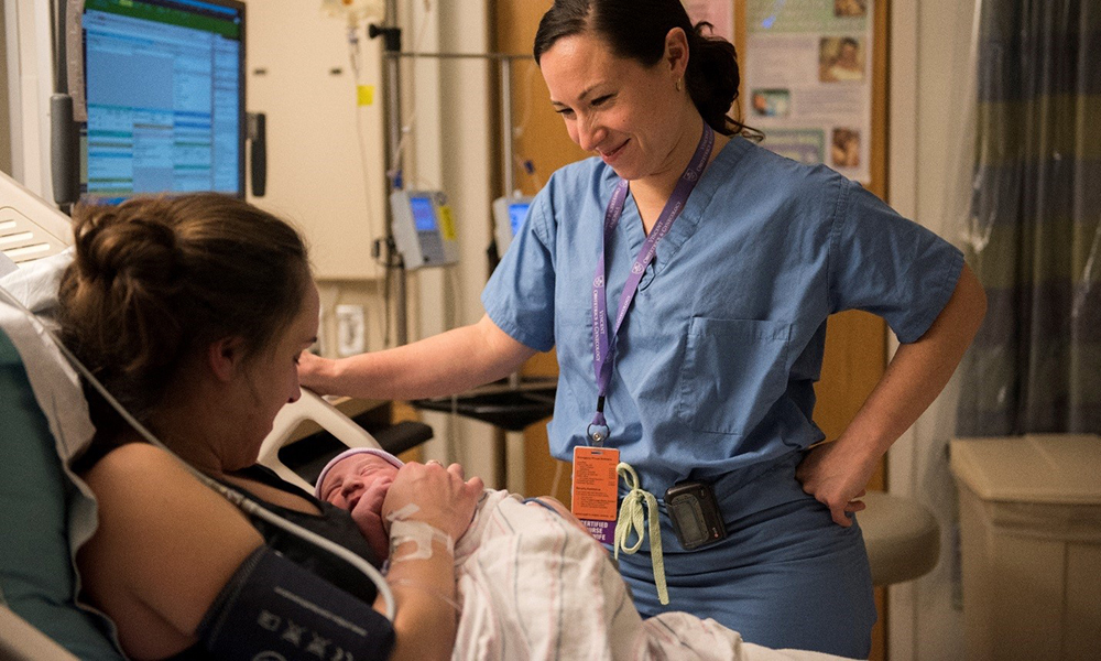 A midwife checks on a mother in bed with her newborn A midwife checks on a mother in bed with her newborn