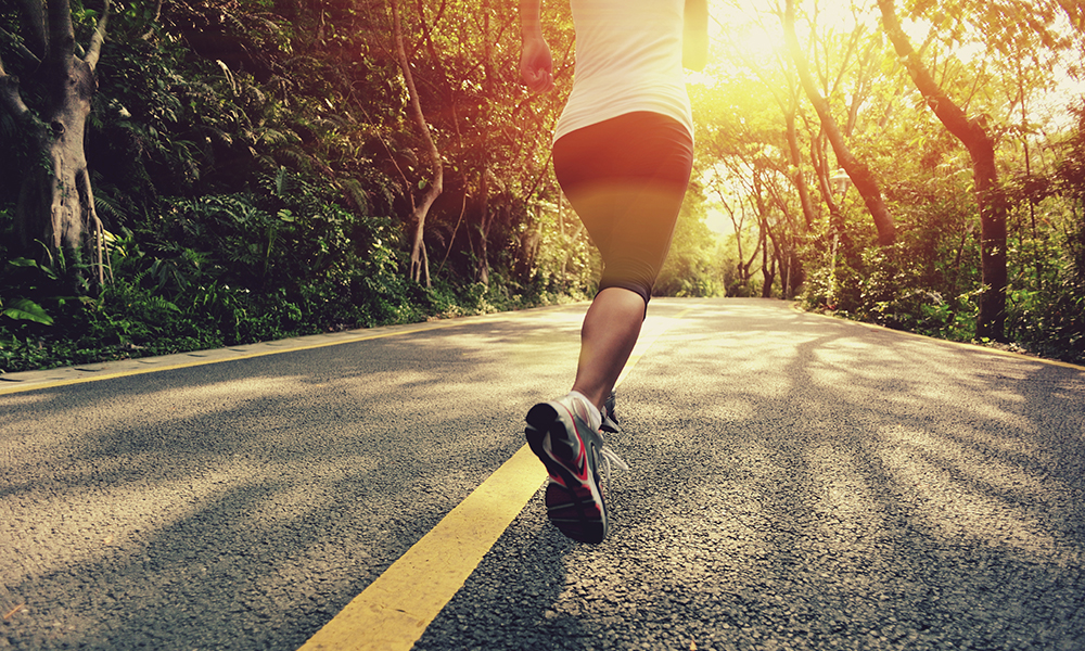 A person runs down a road surrounded by trees A person runs down a road surrounded by trees