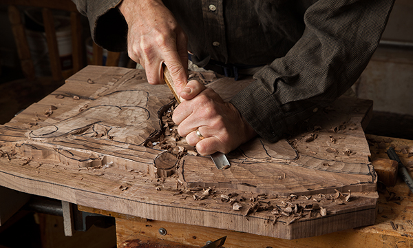 The hands of a woodworker carving a curl of wood out of a sculpture. The hands of a woodworker carving a curl of wood out of a sculpture.