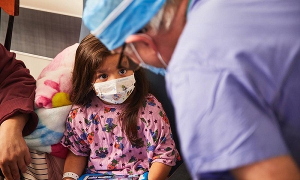 A staff member speaks with a masked pediatric patient A staff member speaks with a masked pediatric patient