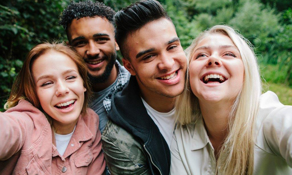 Four teenagers gathered outdoors, taking a selfie. Four teenagers gathered outdoors, taking a selfie.